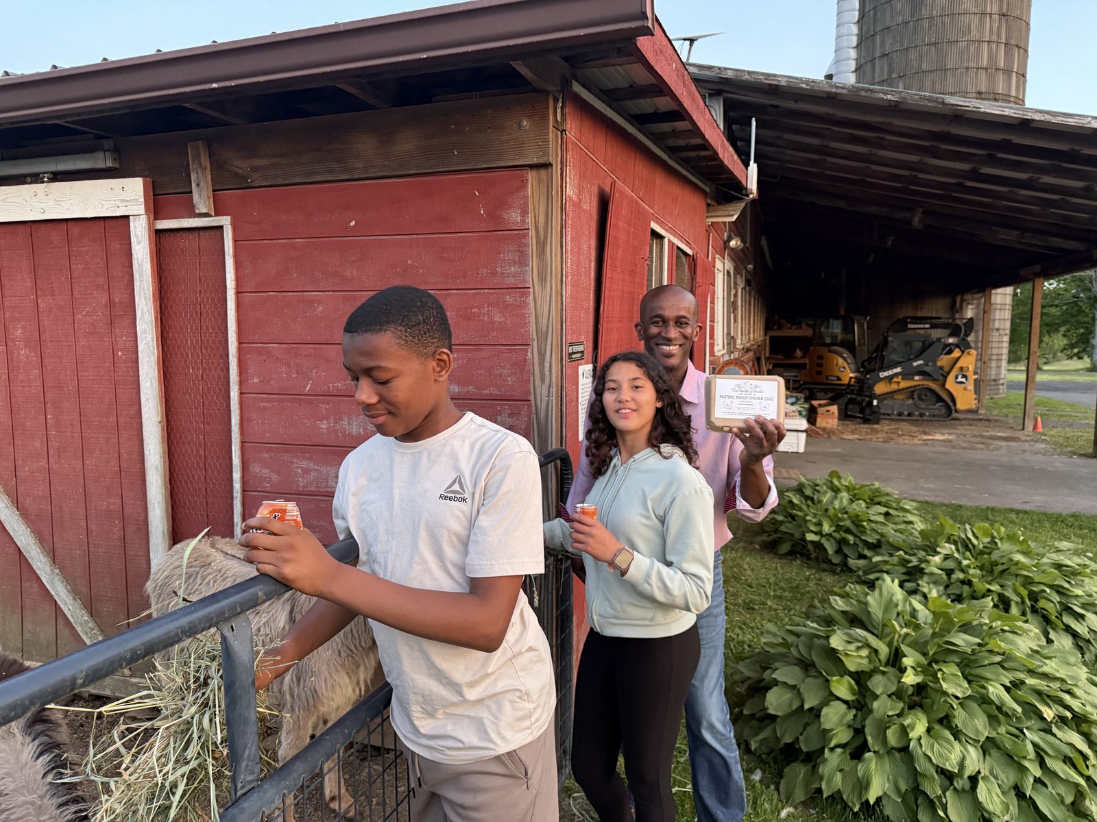 A Council member and two young people at a local farm, holding a carton of pasture-raised eggs